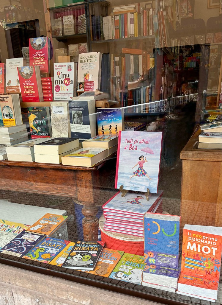 Vetrina di una libreria con una varietà di libri esposti, tra cui romanzi e dizionari.