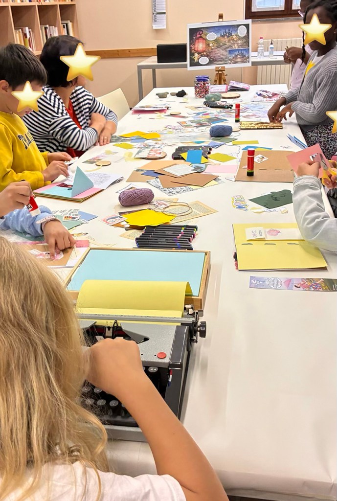 Bambini e adulti che partecipano a un laboratorio creativo, con materiali artigianali sparsi su un tavolo, tra cui carta, colla e una macchina da scrivere.